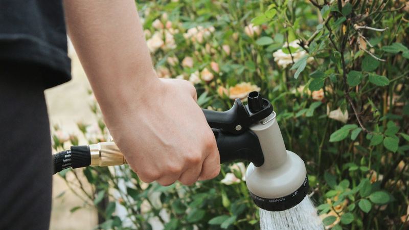 Hand holding a hose nozzle, watering a garden bed